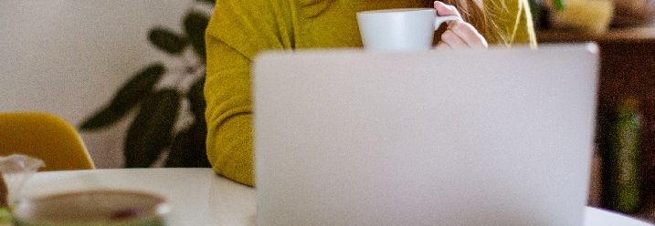 Frau sitzt mit Kaffee vor einem Laptop